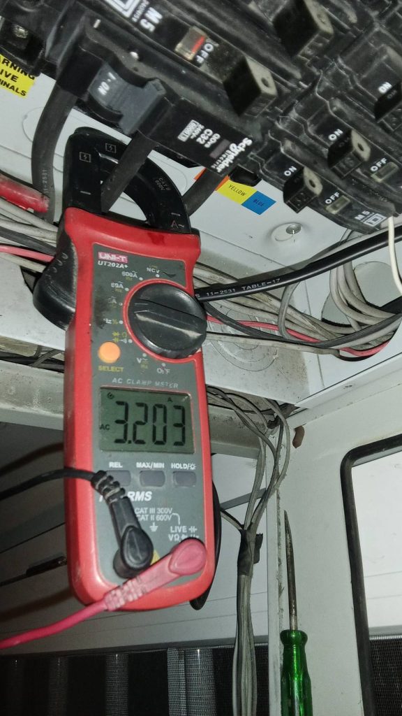 A clamp meter shows a current reading of 3.203 A in an electrical panel.