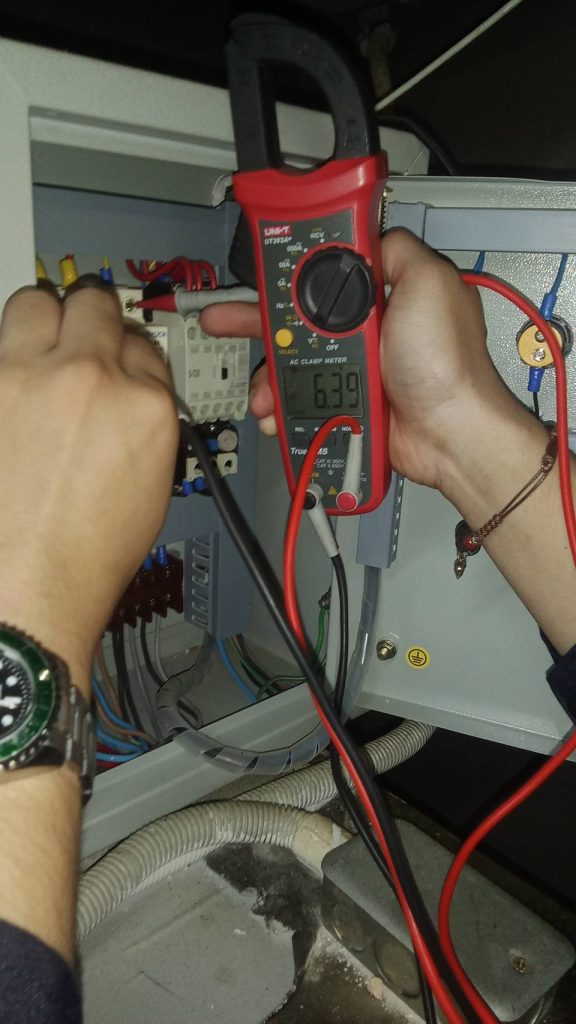 Measuring current with a clamp meter inside an electrical control panel.