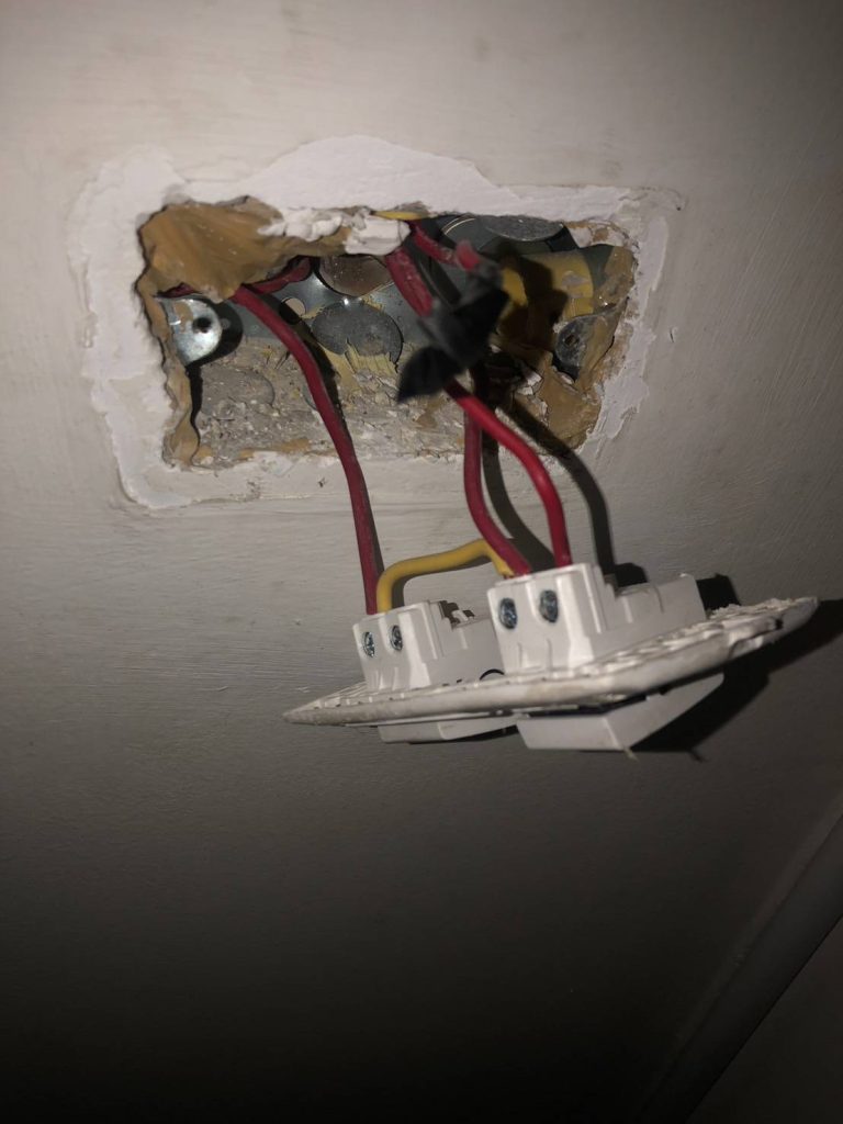 A wall switch with exposed wiring pulled out from the electrical box.